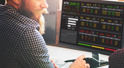 Bearded man wearing checked shirt looking at stocks on a computer screen