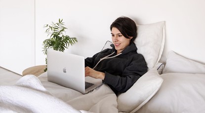 Woman smiling in bed with a laptop