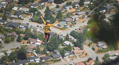 Woman wearing black and yellow striped top balances on a high-wire, with a residential suburb in the background