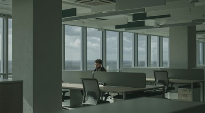 Man sitting alone in a large office building, with many empty desks around him.