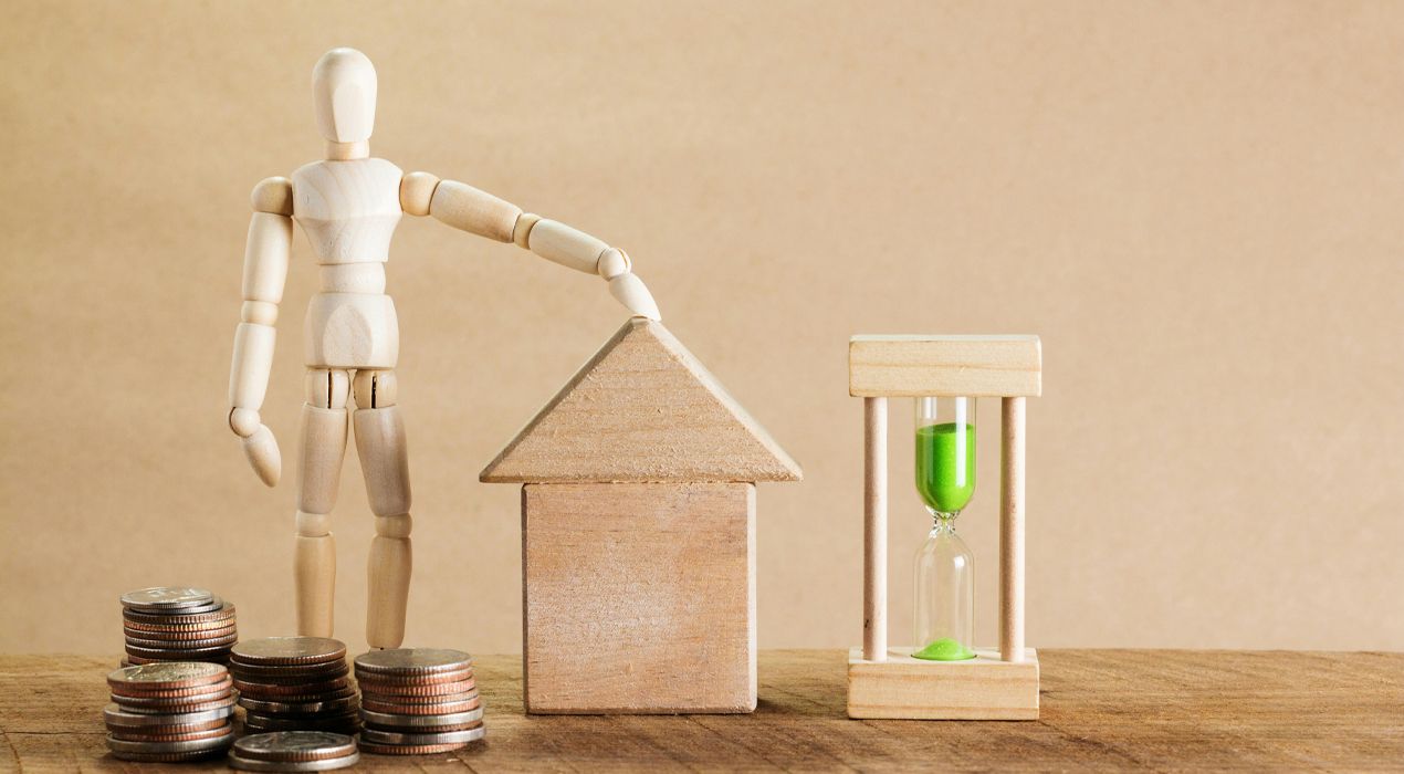 Wooden drawing mannequin standing next to a wood house model and a sand timer. 