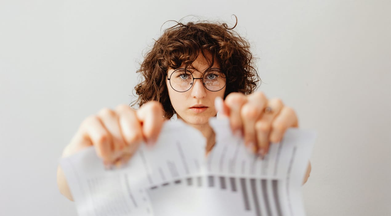 A young person with curly hair and round glasses tearing a piece of paper in half