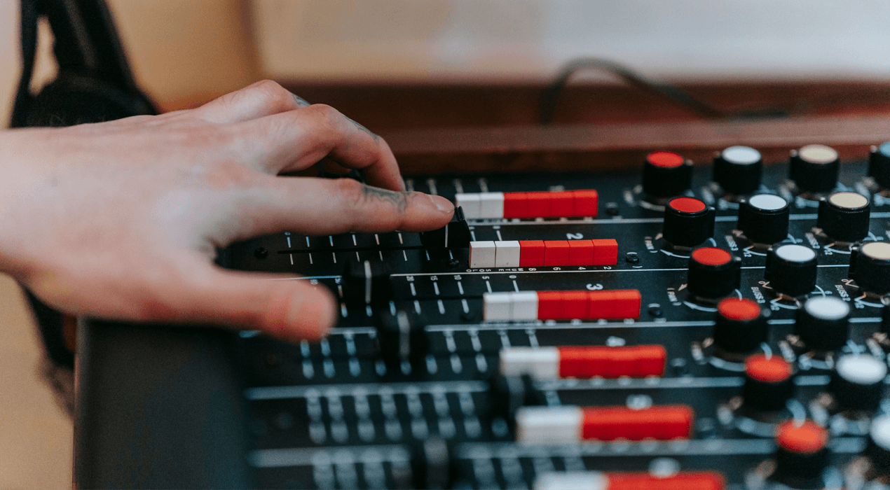 Hand pushing up volume controls on a dj controller / mixer board