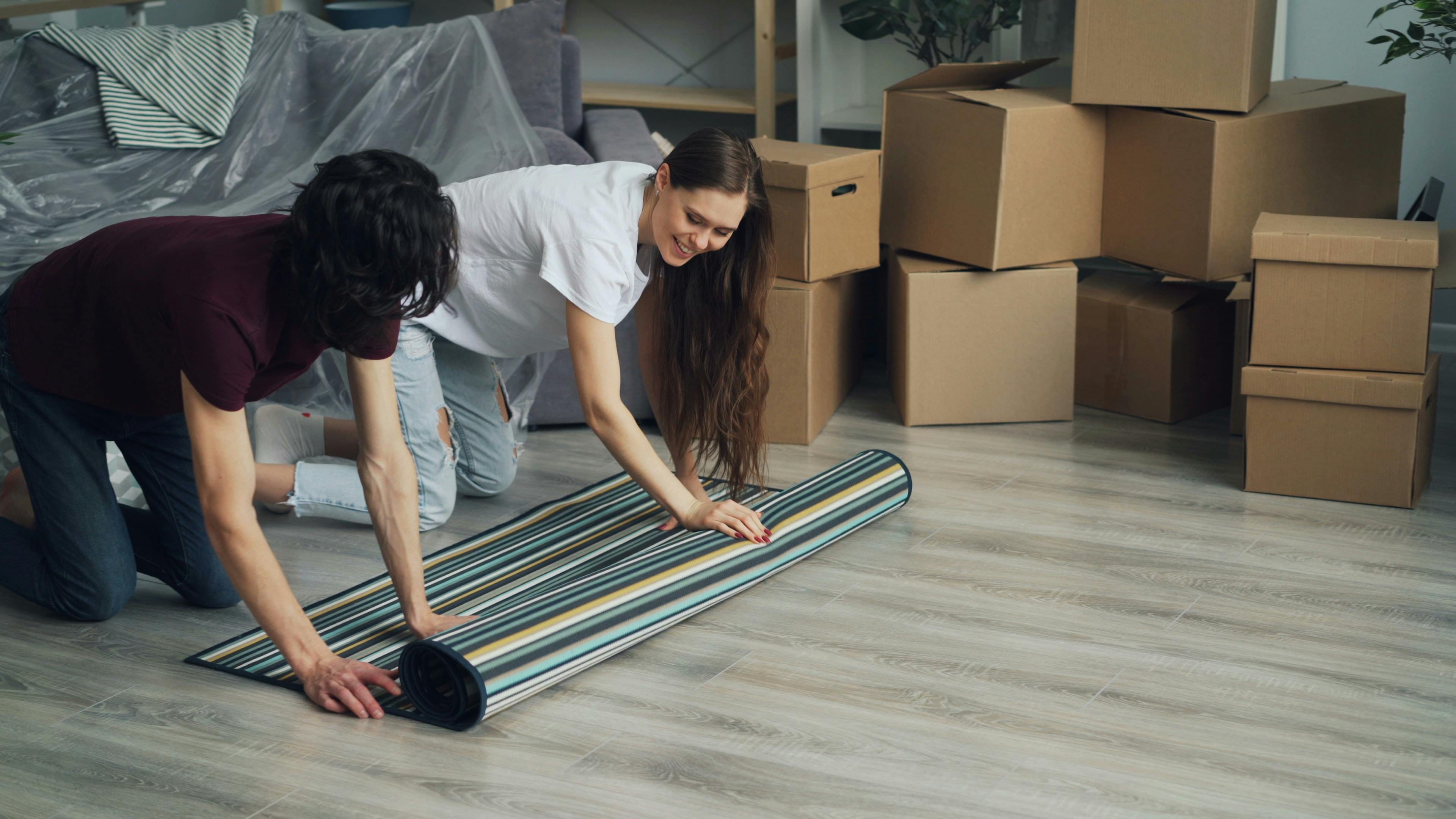 Two young people moving house, rolling out a rug on the floor