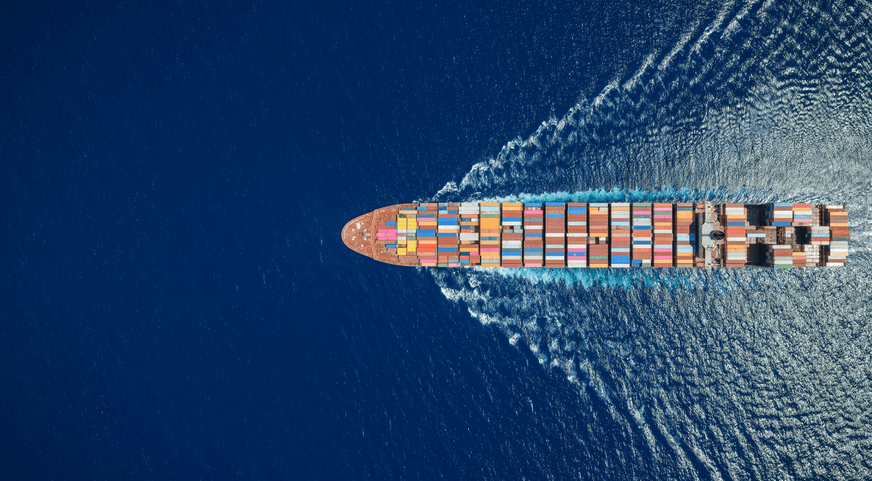 Birds eye view of a container ship in the ocean, wake fanning out to either side