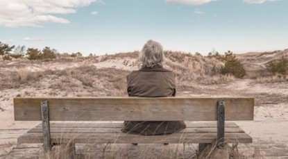 Older person sitting on a bench looking out over the landscape