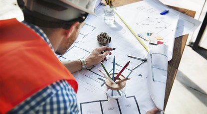 Man wearing hard hat looking over construction drawings on desk