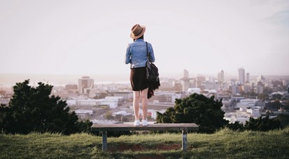 Woman standing on bench on top of hill, looking out at Auckland in the distance