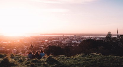 View of Auckland from top of Mt Eden, sun setting with three people in foreground