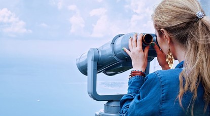 Back view of woman looking through binoculars at the ocean
