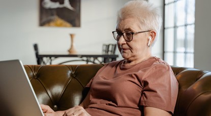 Elderly woman sitting on leather couch looking at laptop