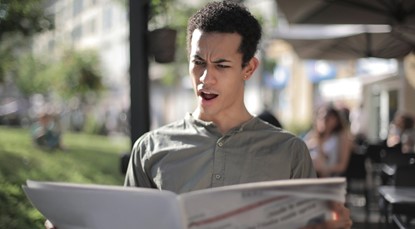 Young man looking shocked at newspaper