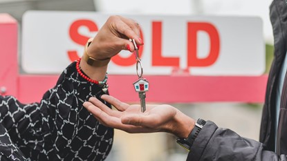 Hand holding house key in front of Sold sign