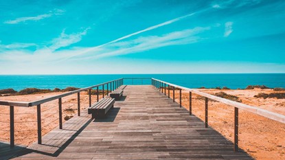 Looking down a wooden boardwalk towards blue ocean on a sunny day.