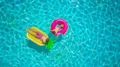 Two young boys on brightly coloured pool floats, floating on clear, sparkling blue water.