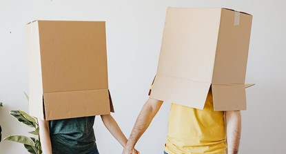 Young couple holding hands with big cardboard boxes over their heads.