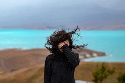 Woman standing on top of a windy hill with hair blowing in face, lake behind her.