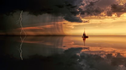 Sail boat sitting on calm water at sunset, with storm building in the distance