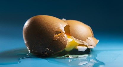 Broken egg sitting on blue surface