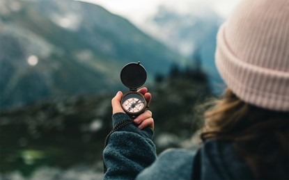 Person holding a magnetic compass, standing in wilderness with mountains in the background