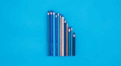 12 blue coloured pencils, all different shades, lined up next to each other on a blue background, starting from longest on the left to shortest on the right.