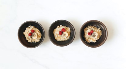 Top view of three bowls of porridge side-by-side, topped with raspberries, banana and chia seeds.