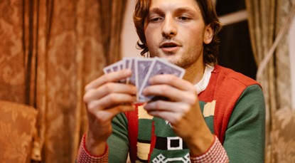 Man wearing Christmas jumper, holding playing cards