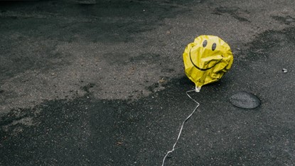 A deflated yellow smiley face balloon laying on concrete.