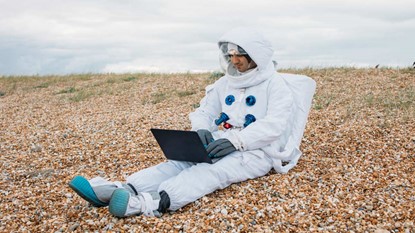 Astronaut sitting on ground with laptop
