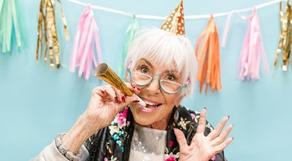 Elderly woman wearing party hat, with party popper